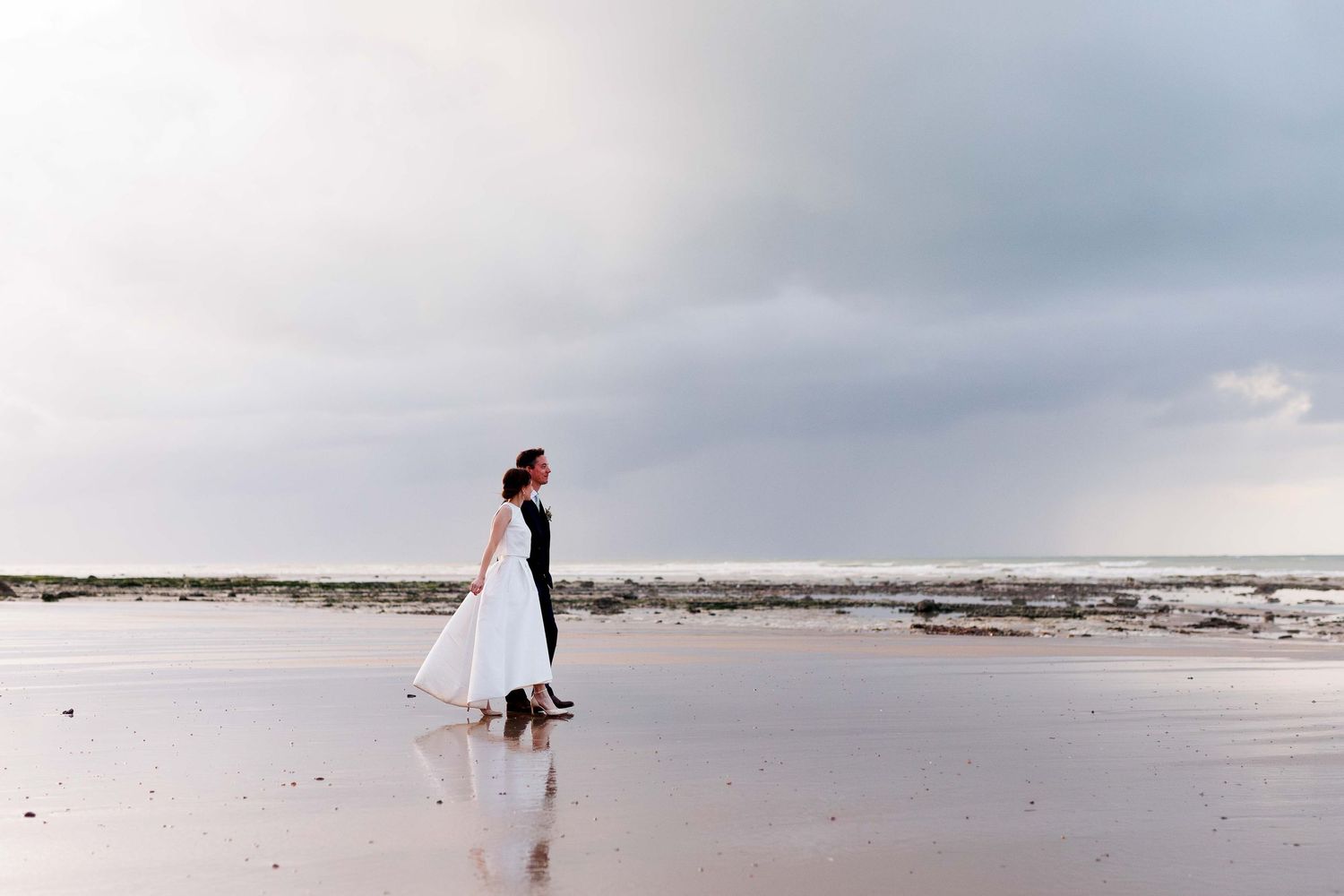 Une silhouette en robe de mariée se dresse, sur le rivage brumeux d'une plage par temps couvert en Normandie au Château de Varengeville