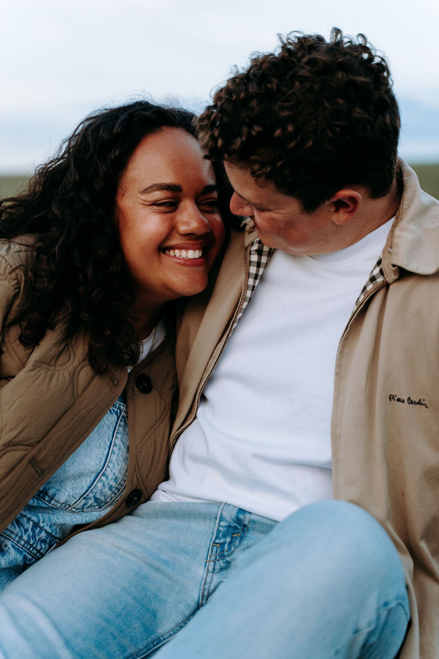 A couple sharing a tender intimate moment outdoors, both wearing casual denim and jackets.