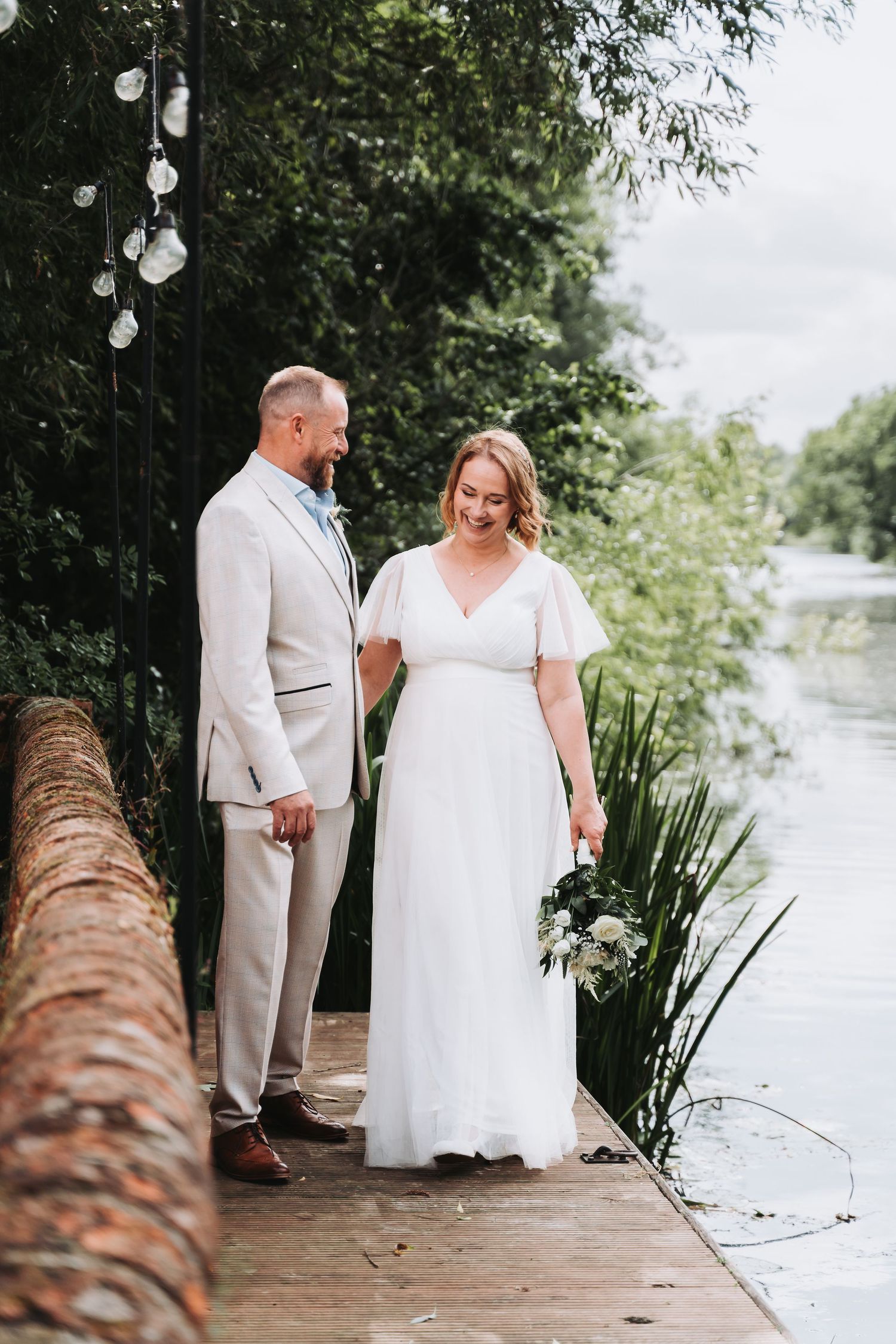 Newlywed couple shares intimate moments during their lakeside wedding photoshoot in white and beige attire.