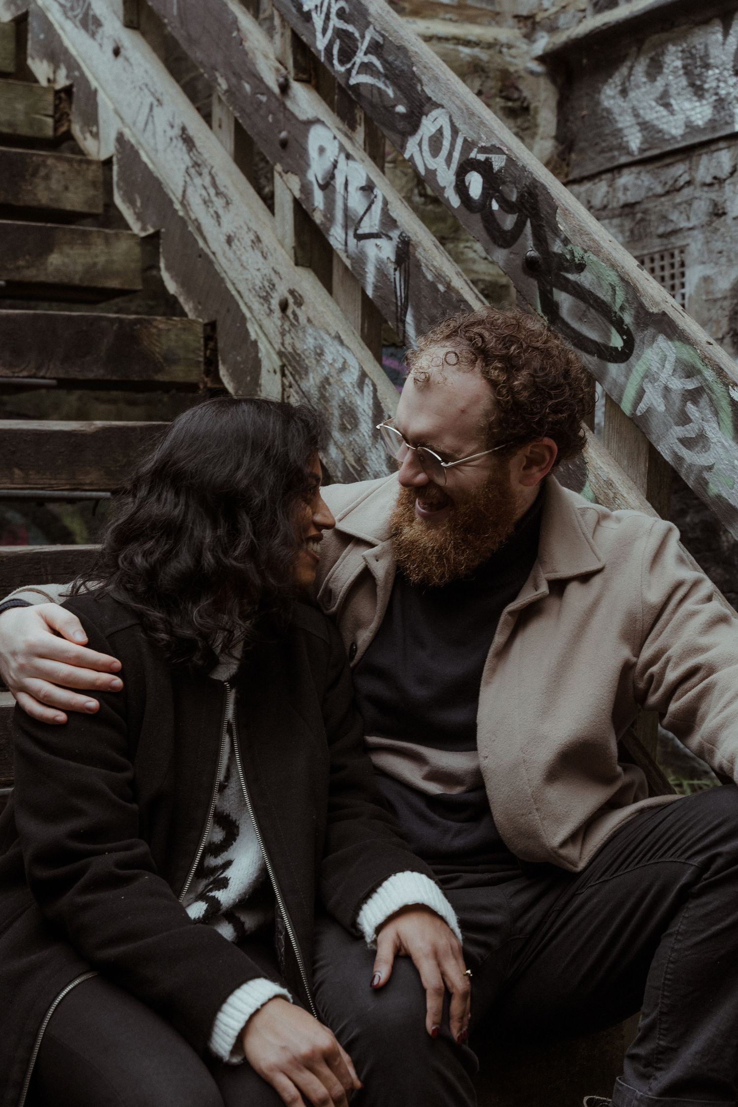 Two people share an intimate moment in a dark, rustic setting with wooden beams and shadows.