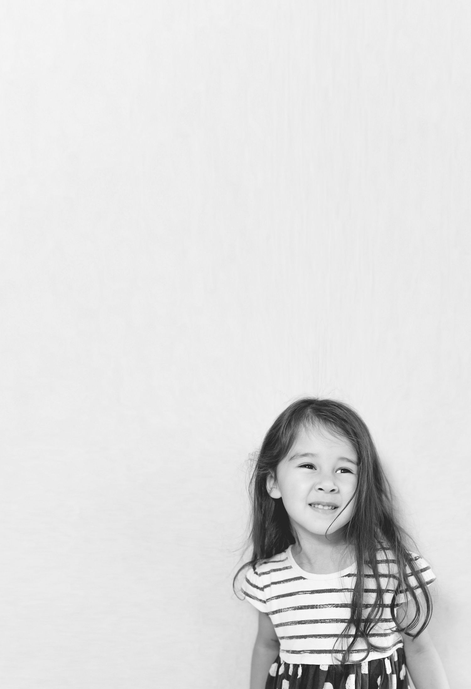 Black and white photo of a smiling young girl with long hair wearing a striped dress against a white background.