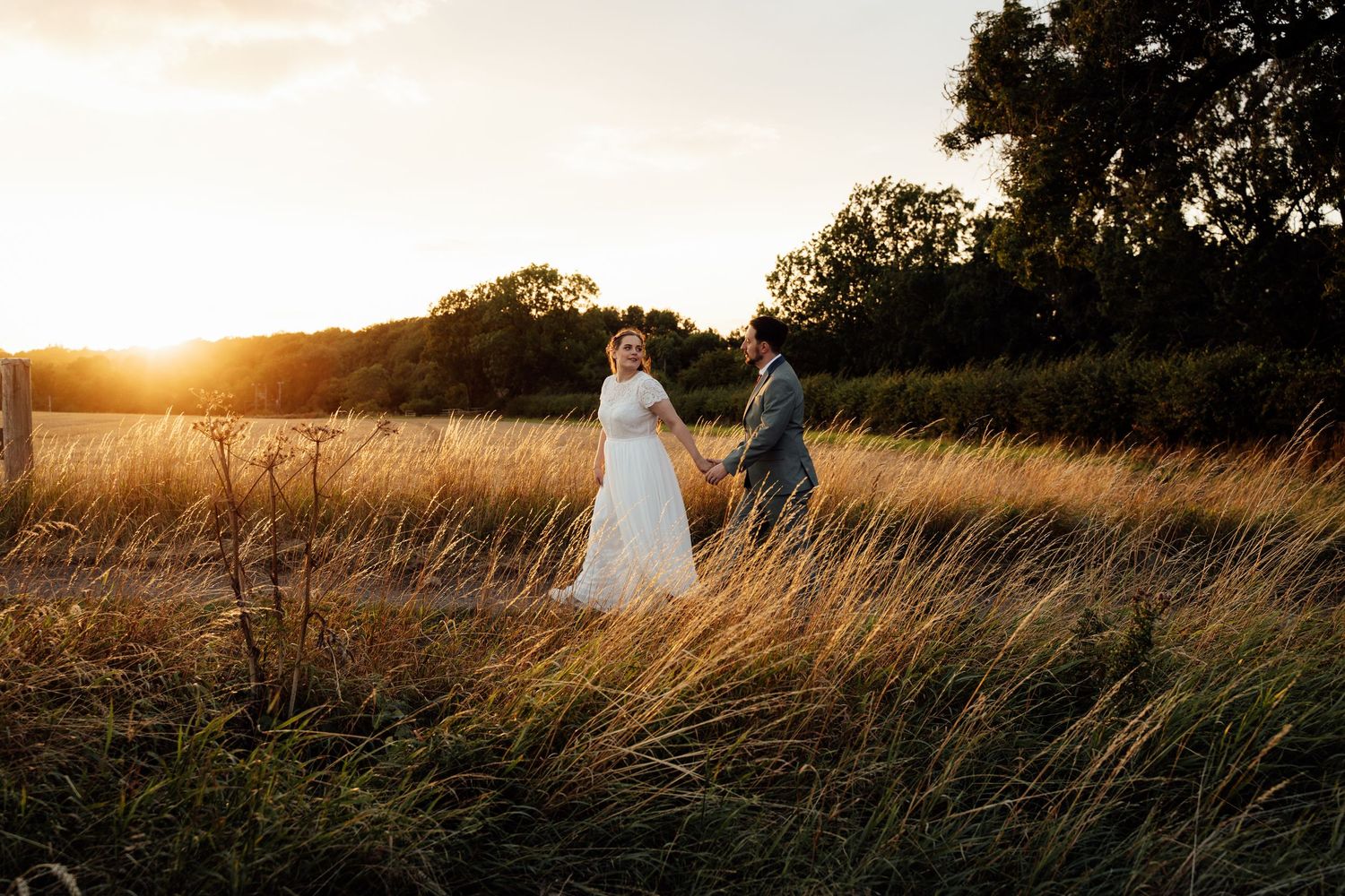 A person in a white dress walks through a golden field at sunset creating a romantic silhouette.