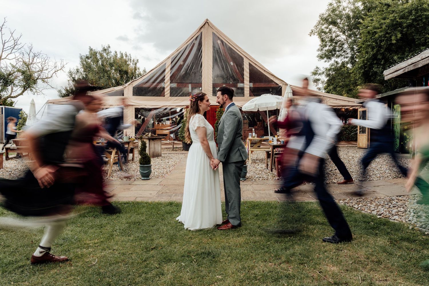Motion blur captures wedding party running and jumping in a playful sequence across an outdoor garden setting.