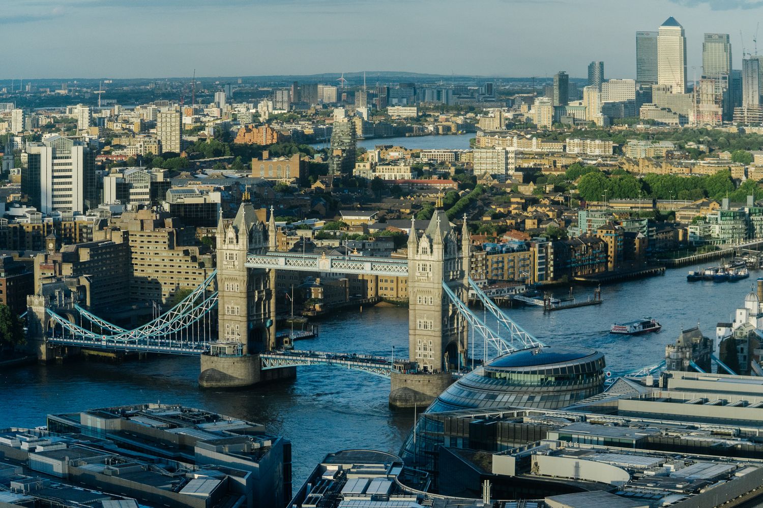 Aerial view of Tower Bridge spanning the River Thames with Canary Wharf skyline in the background, London, UK.