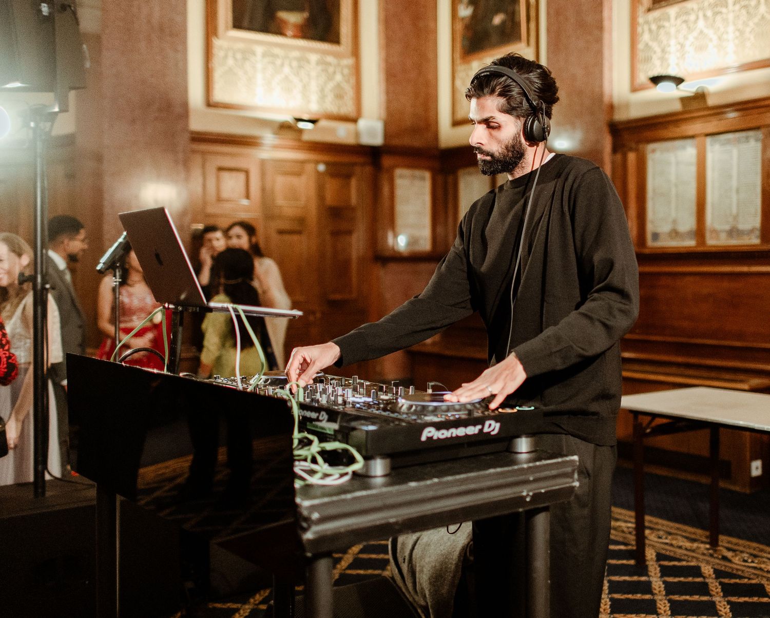 DJ mixing music on Pioneer DJ equipment in an elegant wood-paneled ballroom during a formal event.