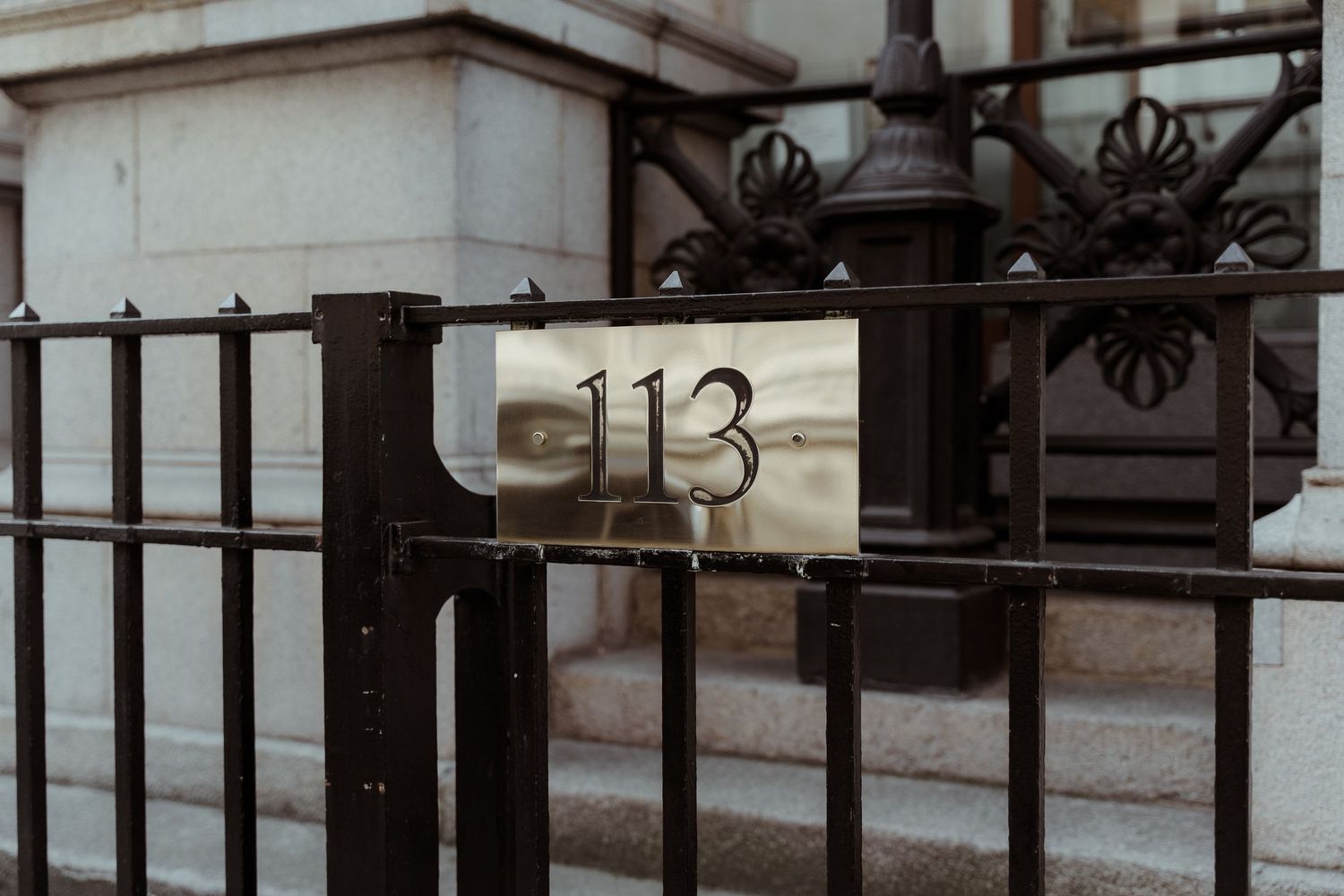 Close-up of a brass number 113 sign on a black wrought iron gate outside a stone building. 113 Chancery Lane, London