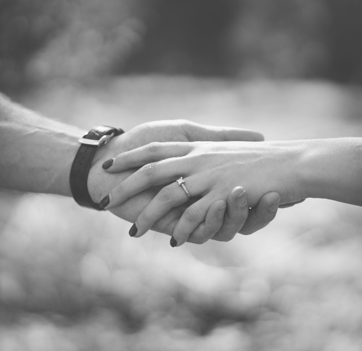 Black and white photo of two people shaking hands, one wearing a bracelet and the other a diamond ring.