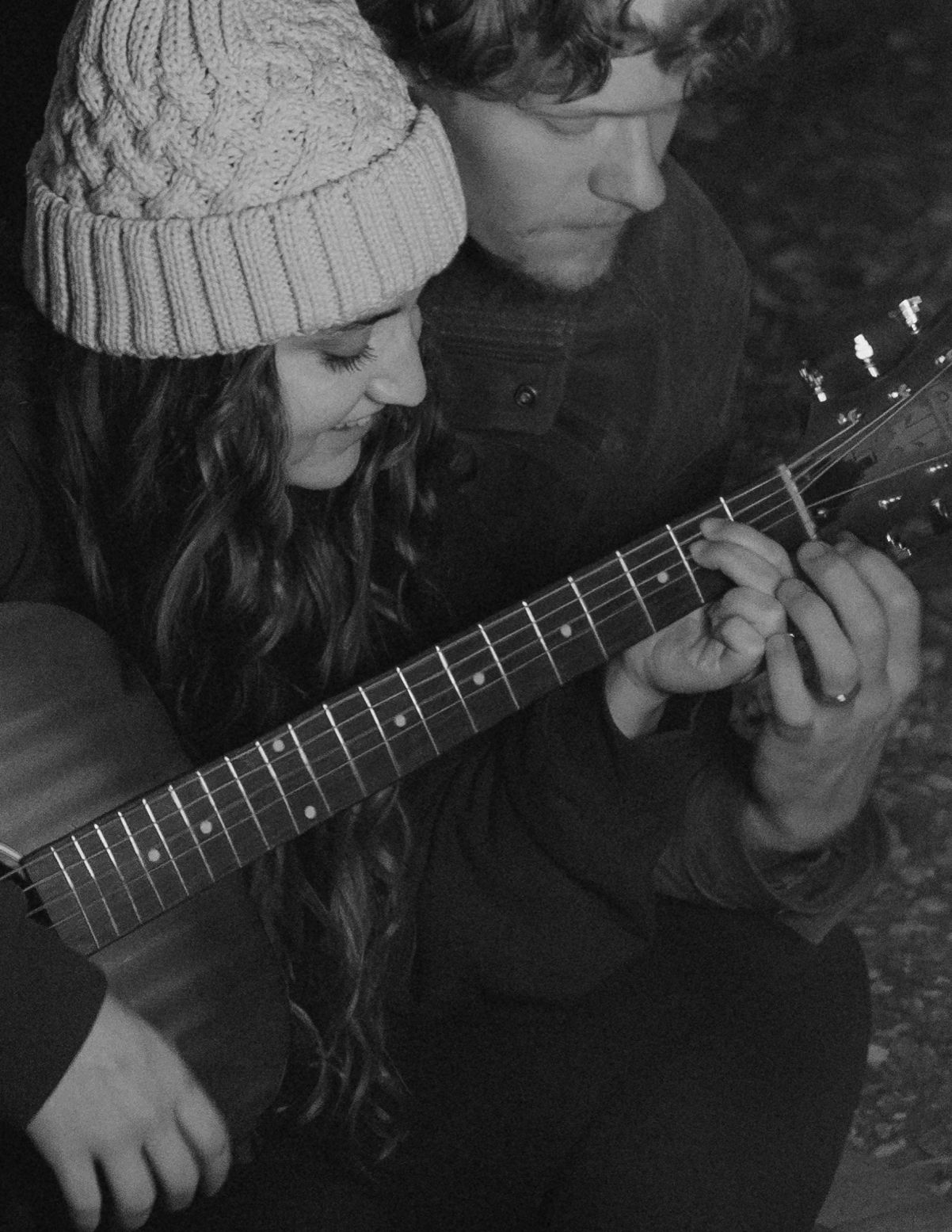 Close-up black and white photo of a man and woman playing guitar together.