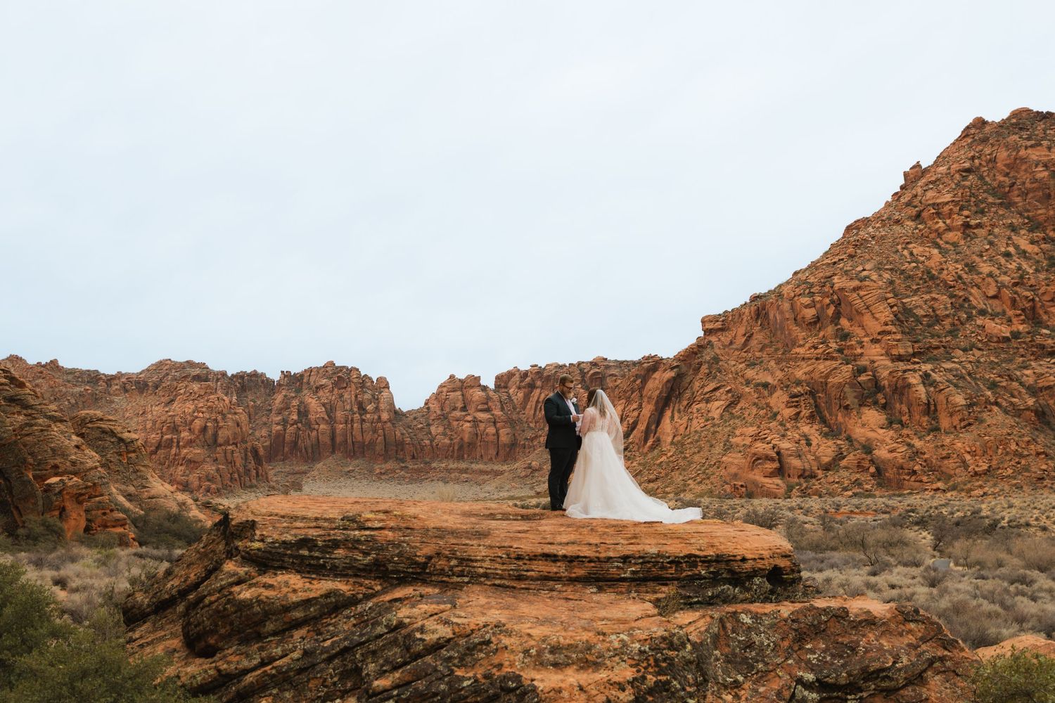 Couple eloping and exchanging vows in the distance, surrounded by breathtaking red rock formations.