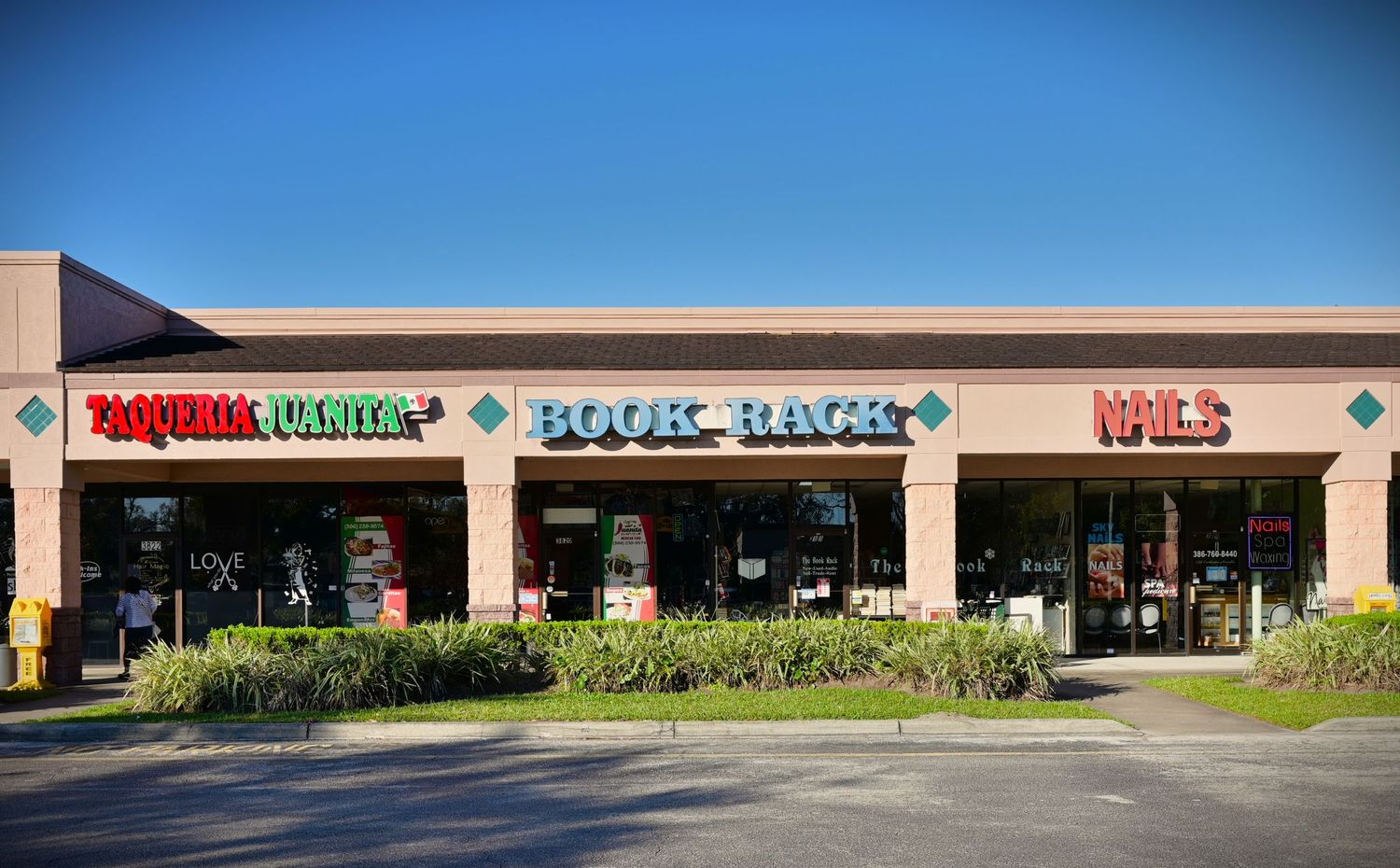 Strip mall shopping center facade with retail storefronts (including Book Rack) and signage during daytime.