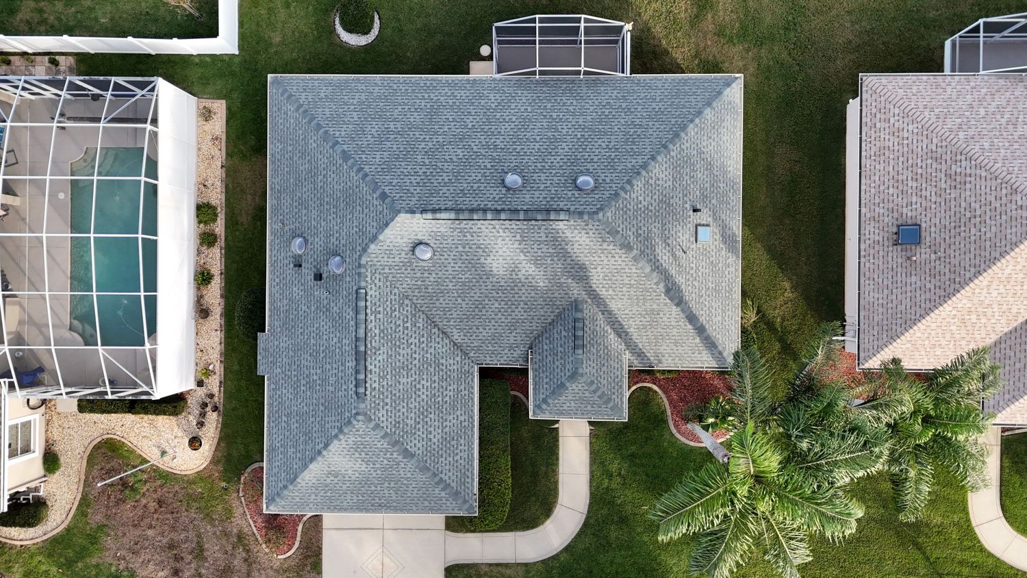 Top-down drone shot of a gray-roofed house with geometric architectural details and palm tree landscaping.