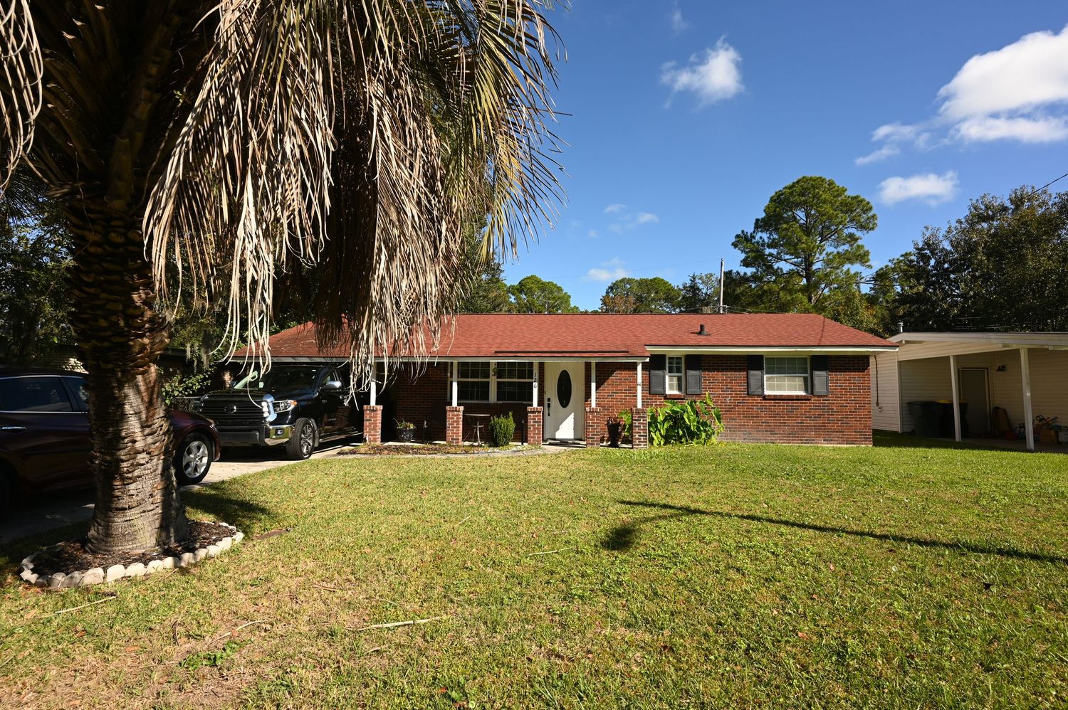 Single-story brick ranch house with red roof and large palm tree in spacious front yard.