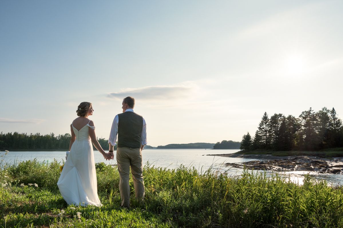 A Burlington, VT, bride and groom are photographed holding hands, overlooking the waters of Maine during their destination wedding