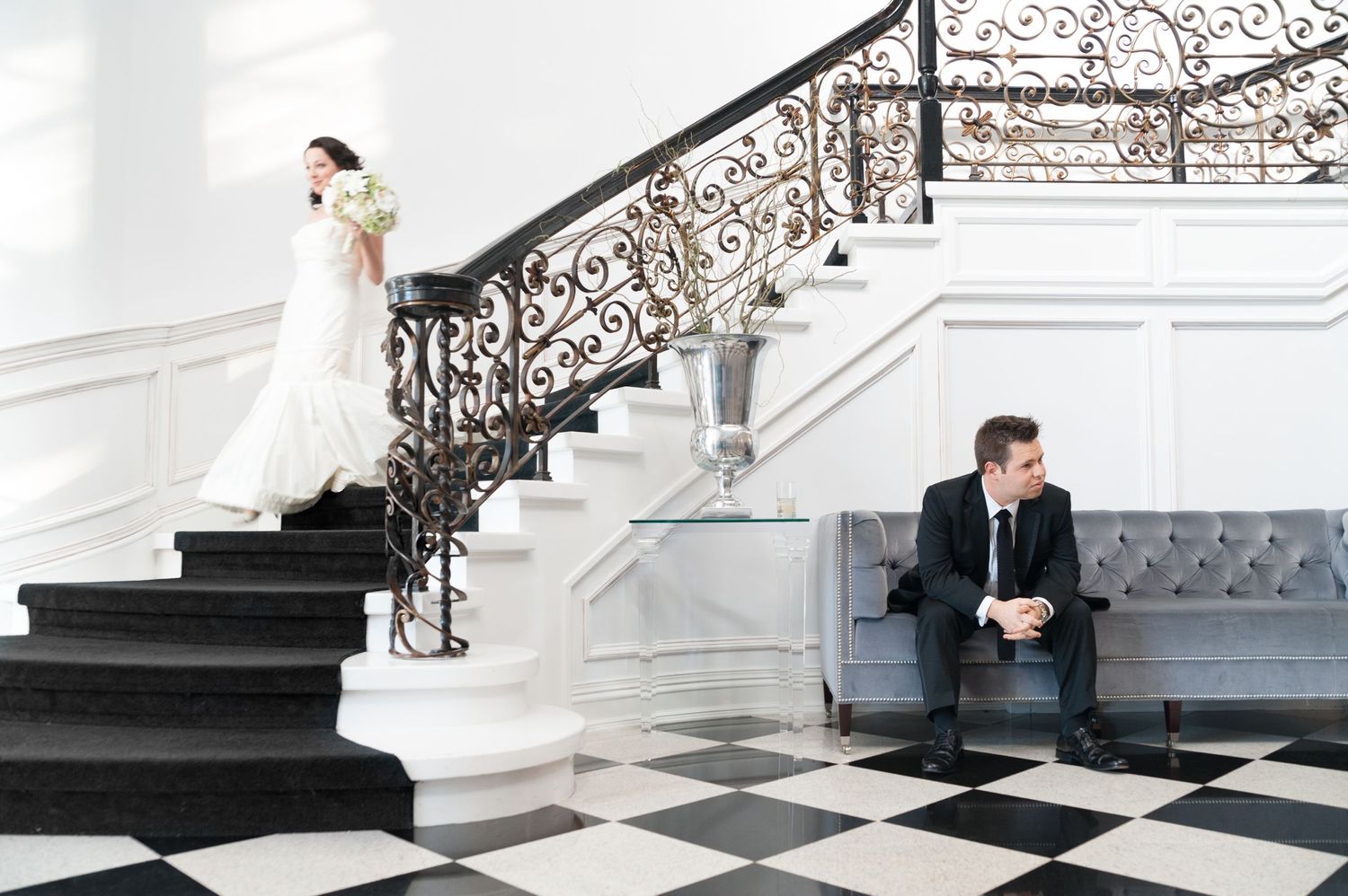 A groom anxiously awaits the first look of his bride on their wedding day, as she descends the stairs at a luxurious wed