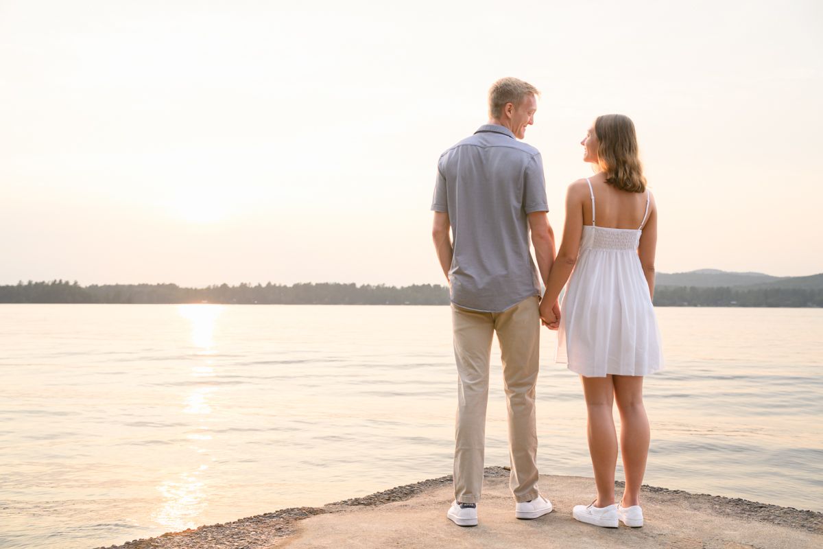 A young couple hold hands during their sunset engagement proposal on Lake Pleasant, near Speculator, NY, in the heart of the Adirondacks