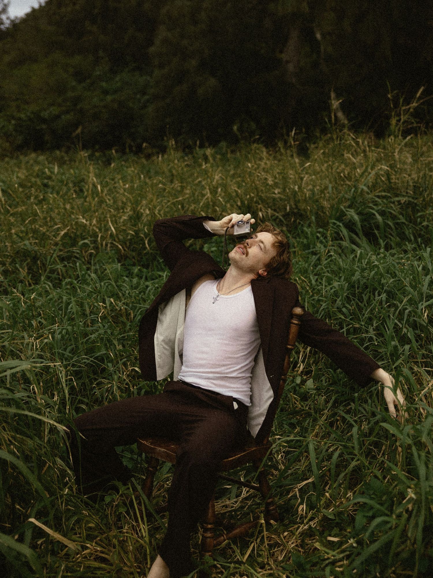 A person wearing a white shirt and brown pants lies back in tall grass during golden hour lighting.