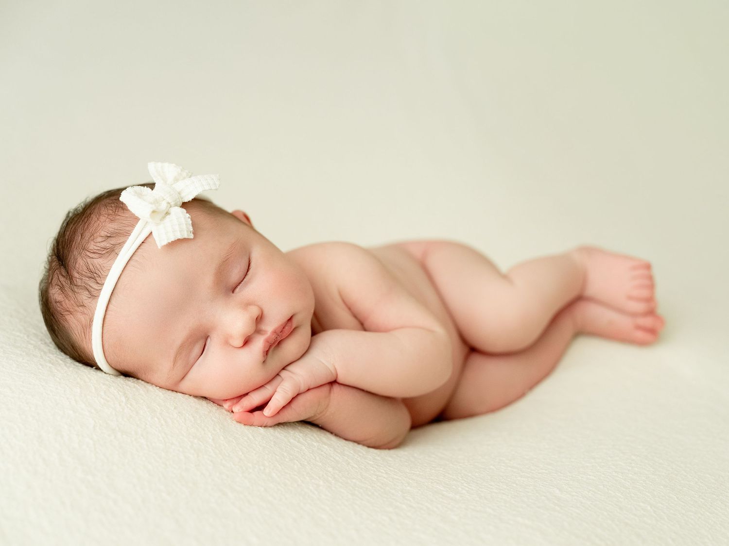 Sleeping newborn baby in white wrap photographed from different angles on cream background.