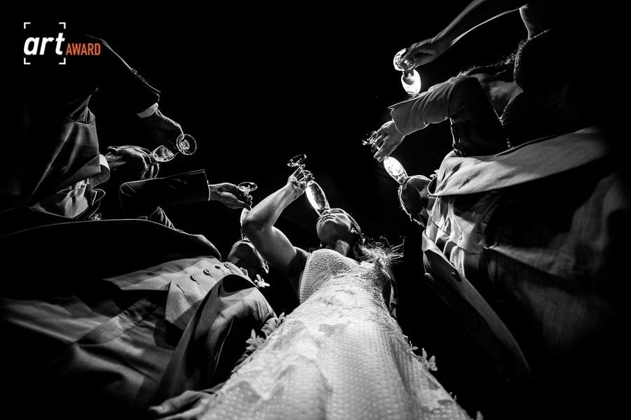 Dramatic low-angle black and white shot of bride surrounded by wedding party raising hands skyward.