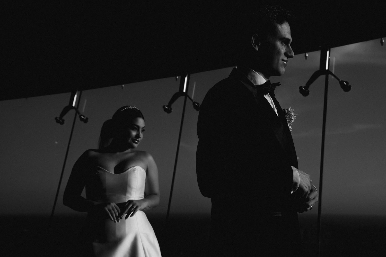 Dramatic black and white silhouette of a bride and groom standing apart in moody wedding portrait.