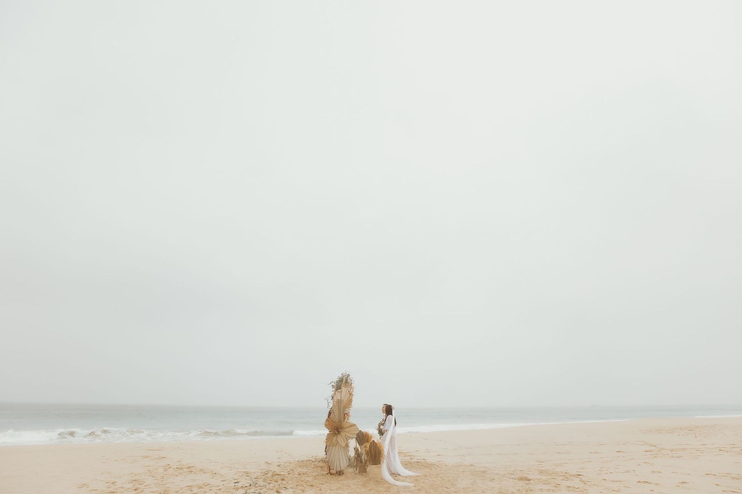 Couple in wedding attire on a misty beach with sandy shores and calm ocean waves in the background.