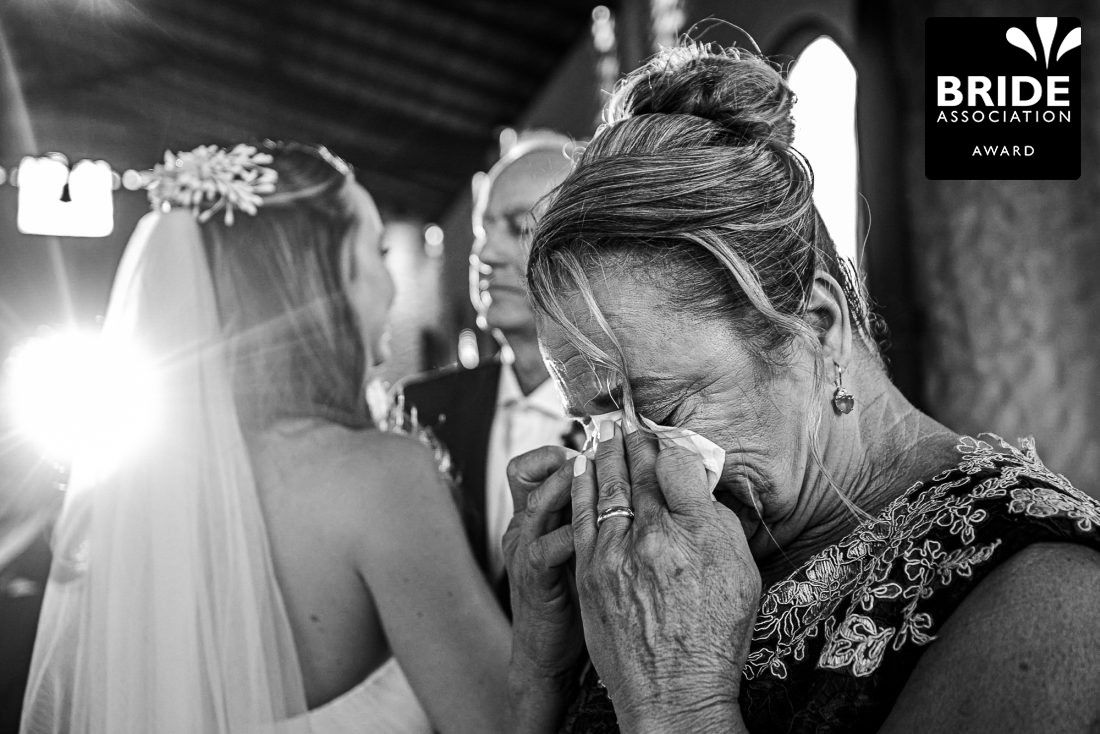Black and white wedding photo of emotional mother wiping tears during ceremony, bride beside her, Bride Association Award winner.