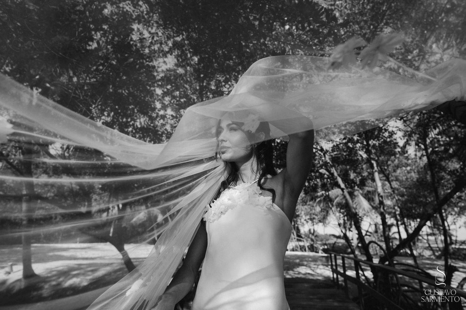 Black and white artistic photo of bride with veil billowing around her face outdoors.