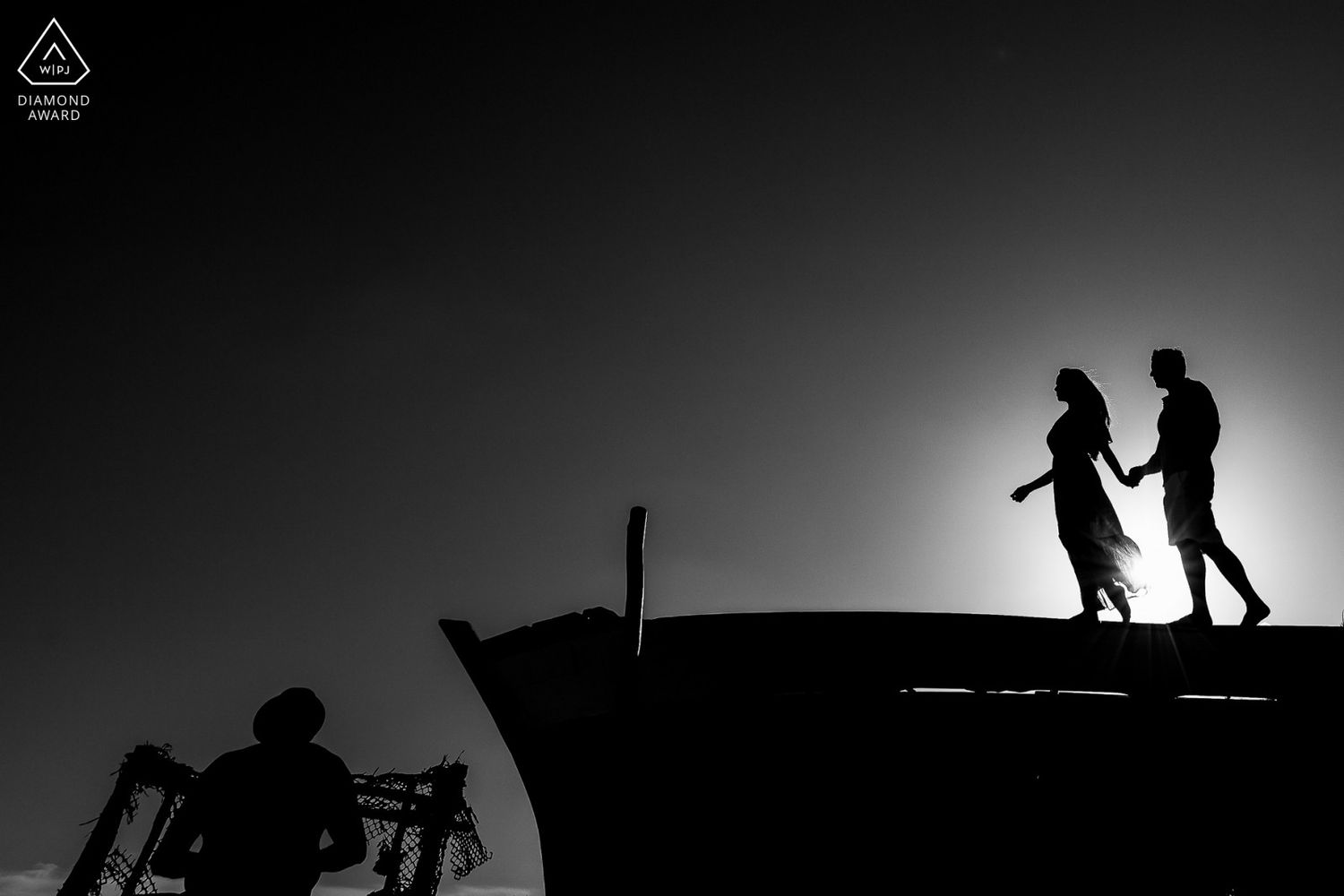Silhouette of a couple holding hands on a rooftop at sunset in black and white.