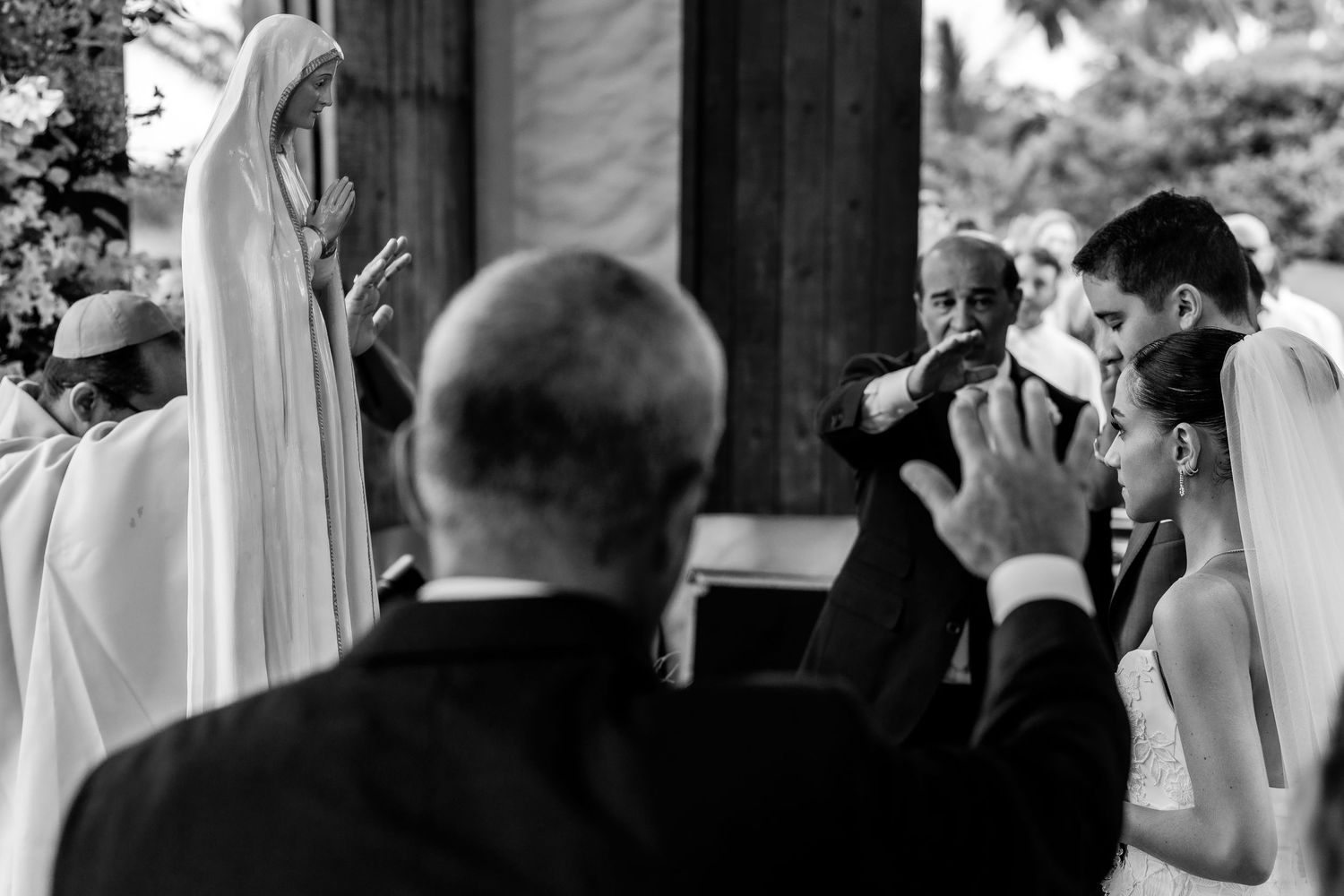 Black and white photo of bride and groom sharing an intimate moment near a religious statue.