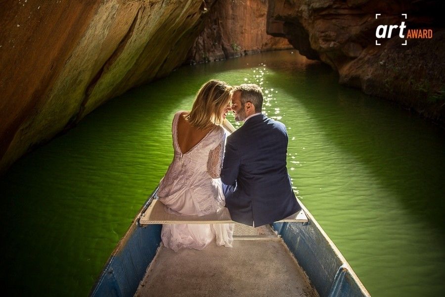 Couple sharing a romantic moment on a boat in a cave with glowing green water, captured for an art award.