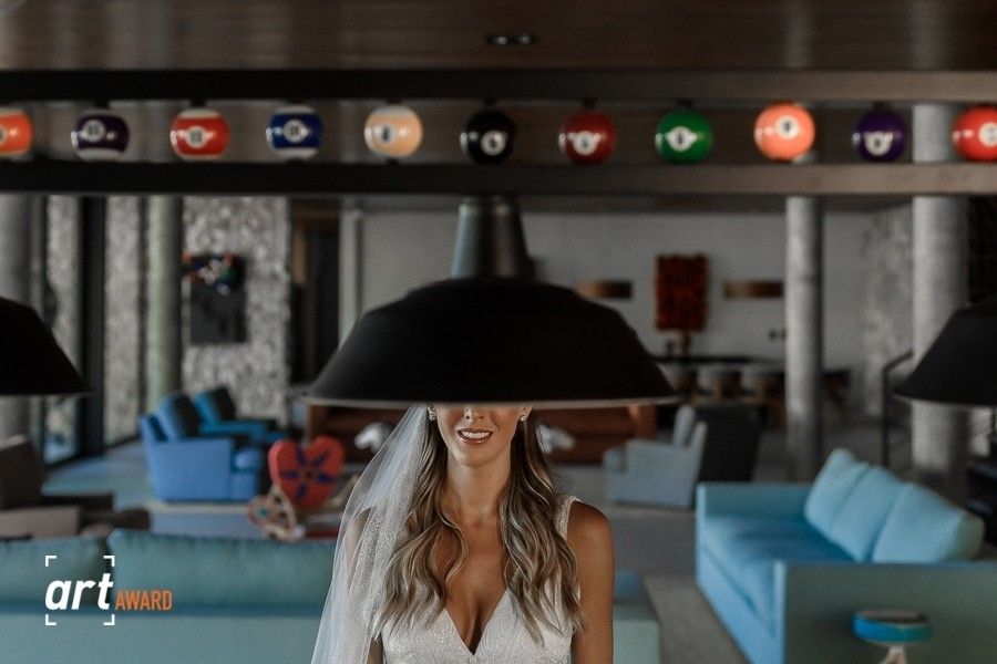 Smiling bride in white dress standing under black pendant lamp with colorful billiard balls display in elegant venue.