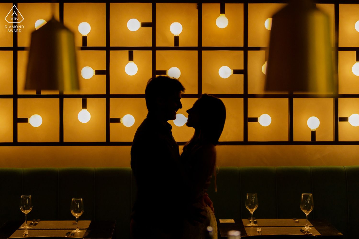 Silhouette of a couple sharing a romantic moment in a warmly lit restaurant with glowing square wall panels.