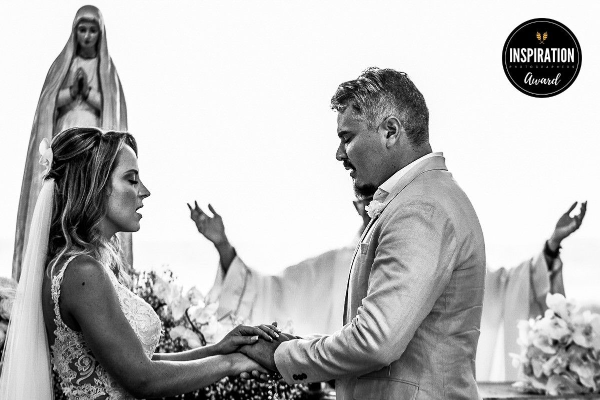 Black and white wedding ceremony photo of couple exchanging vows before a Virgin Mary statue, captured by Inspiration Loved.
