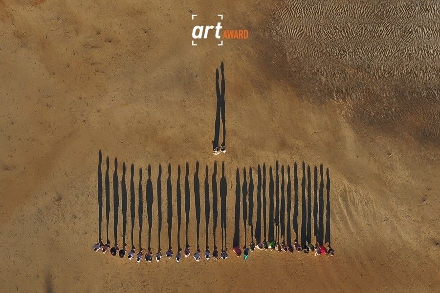 Aerial drone view of wedding party casting long shadows while standing in a line on sandy terrain.
