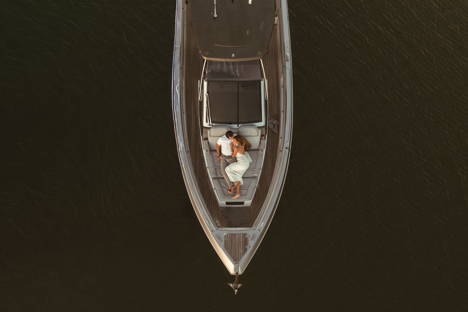 Bird's eye view of a couple relaxing together on a sleek white sailboat on dark tranquil water.