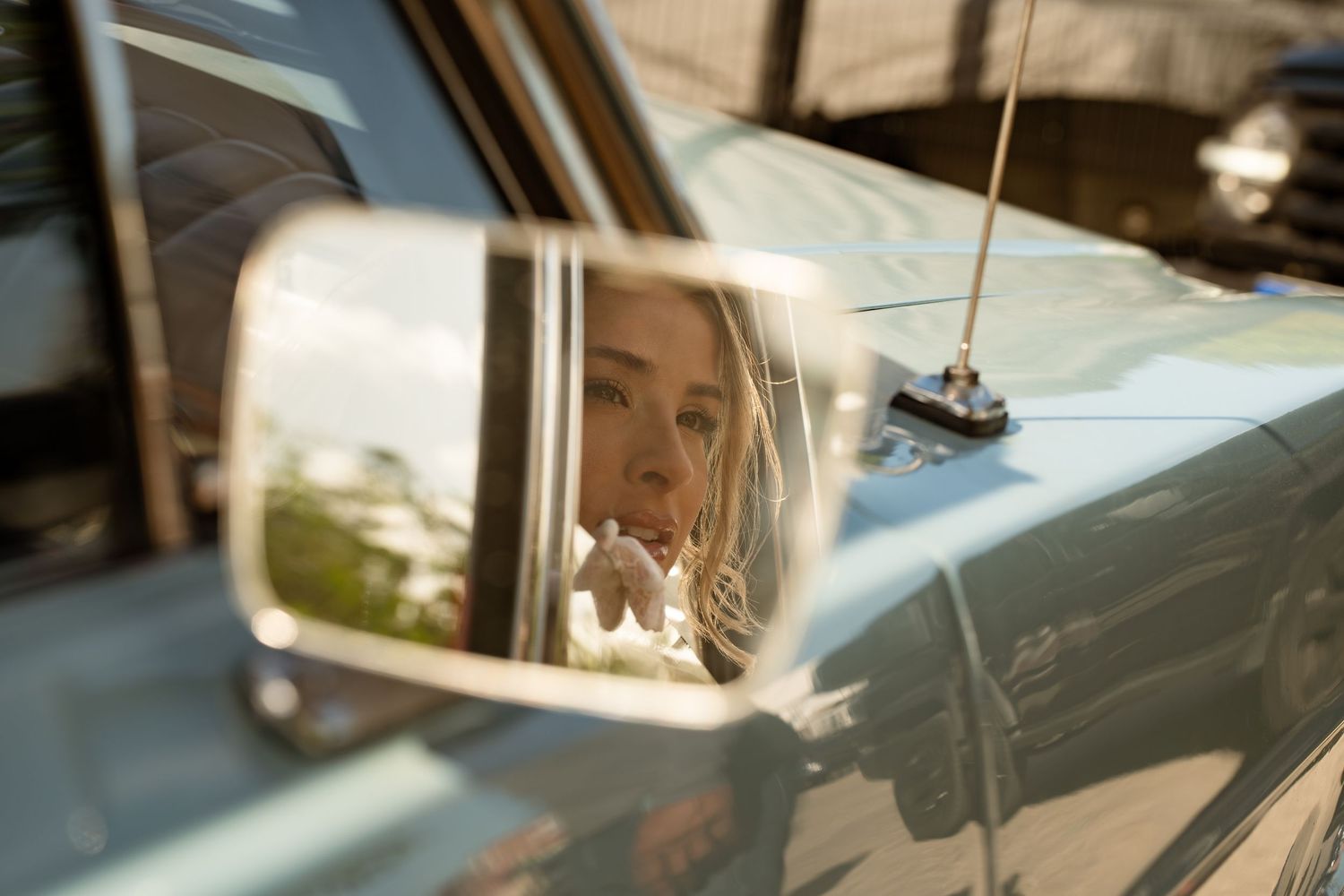 Woman's reflection visible in vintage car side mirror on sunny day.