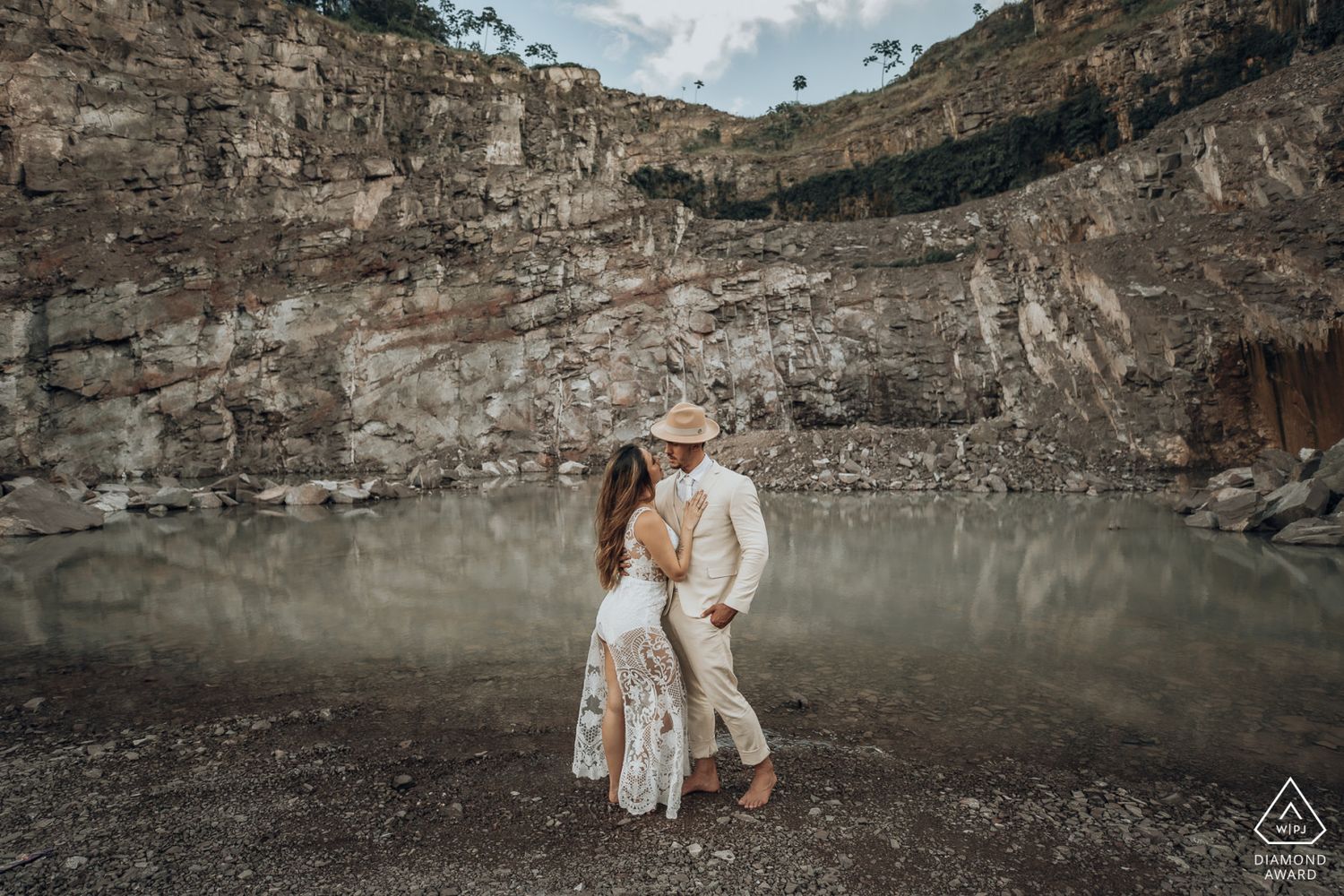 Couple kissing in front of a rocky quarry lake in matching white boho outfits.