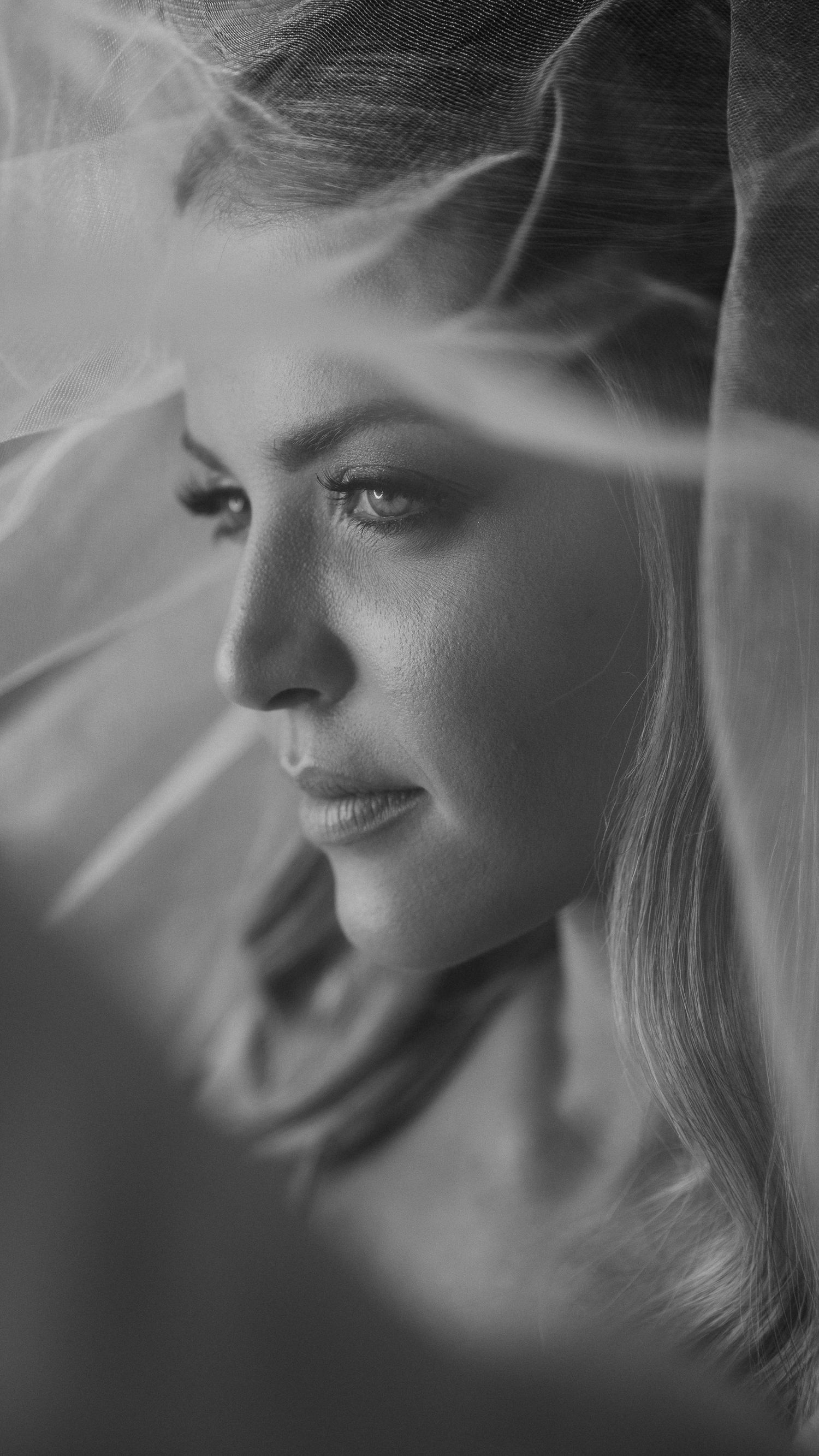 Elegant black and white portrait of a blonde bride draped in a soft flowing wedding veil.