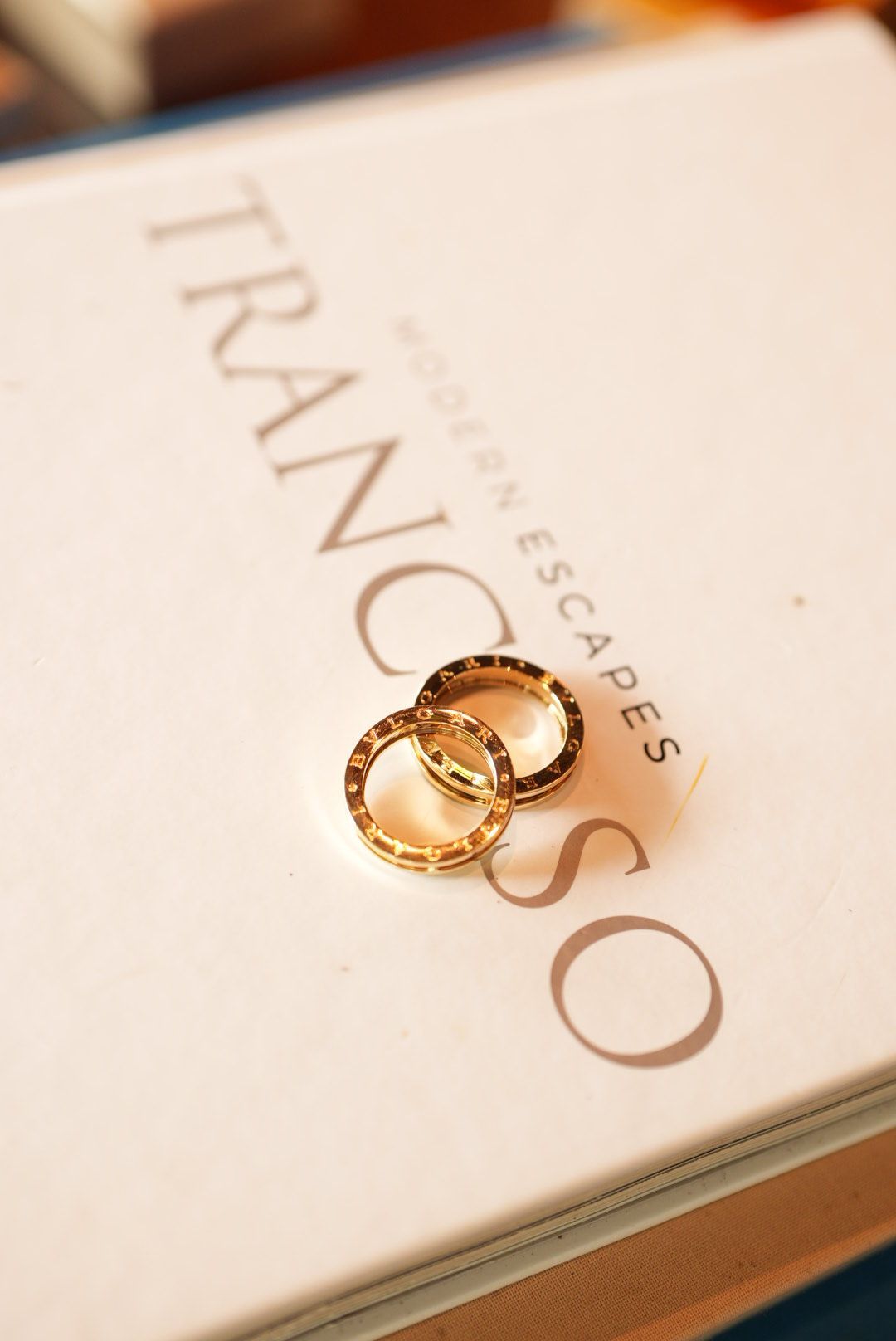 Two gold wedding bands resting on a Trancoso Modern Escapes book, elegant ring photography.