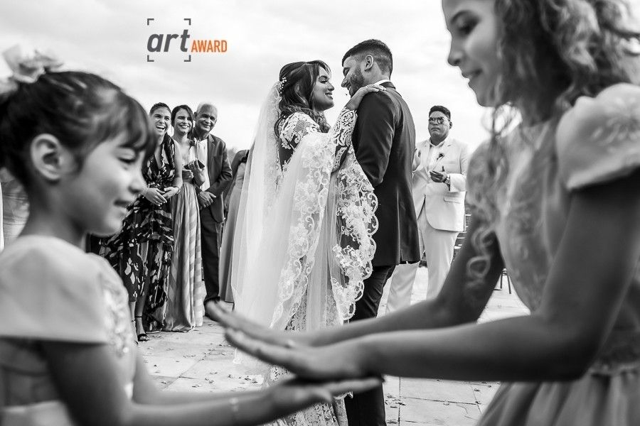 Black and white wedding photo of bride and groom exchanging vows outdoors with flower girls and guests.