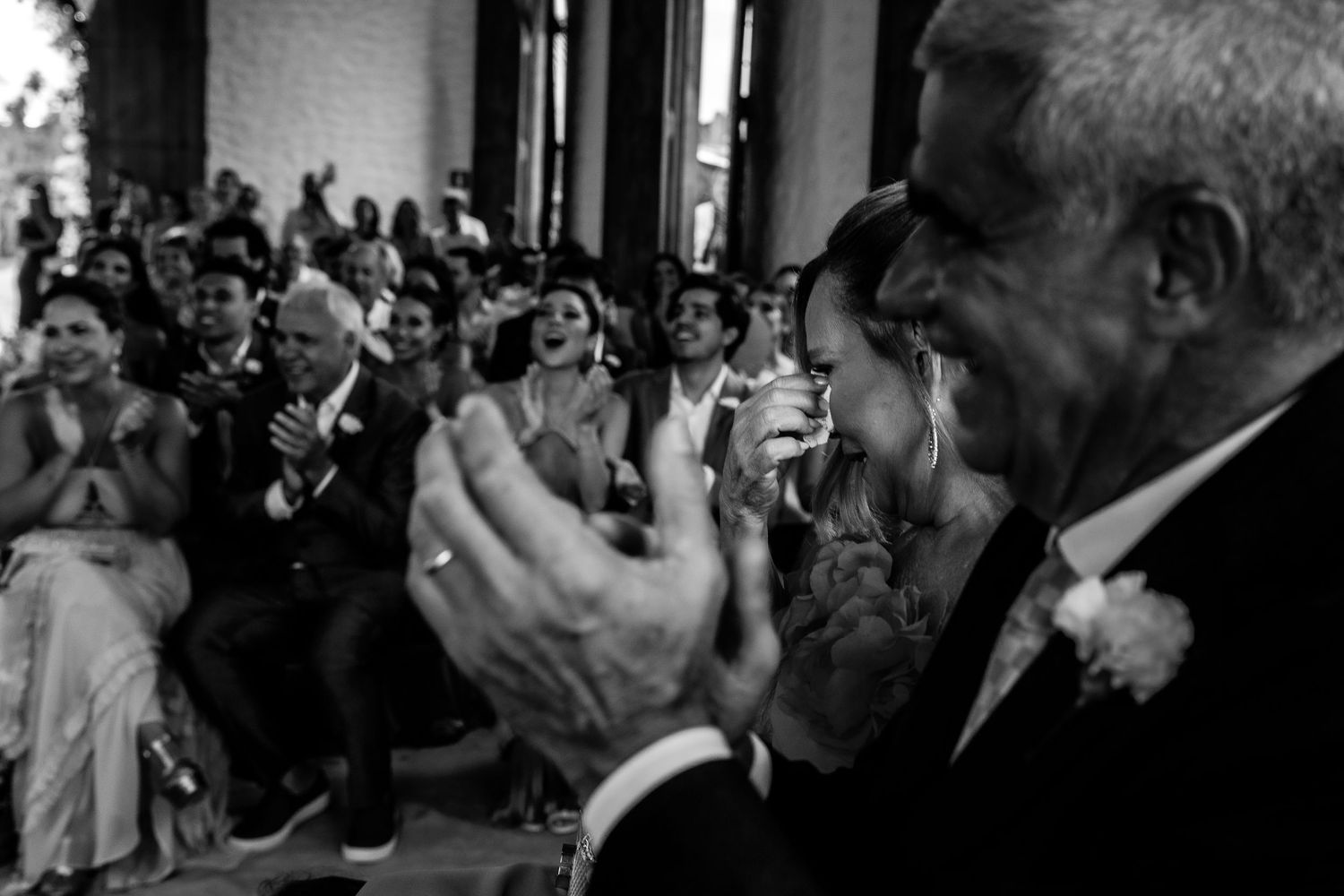 Black and white photo of wedding guests clapping and celebrating joyfully during the ceremony.