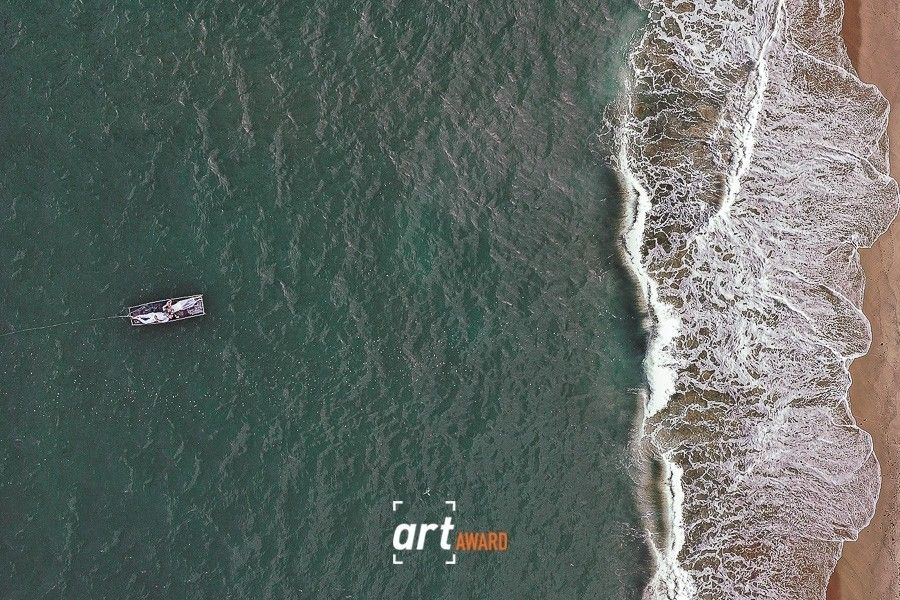 Aerial drone view of a surfer paddling in turquoise ocean waves near sandy beach.