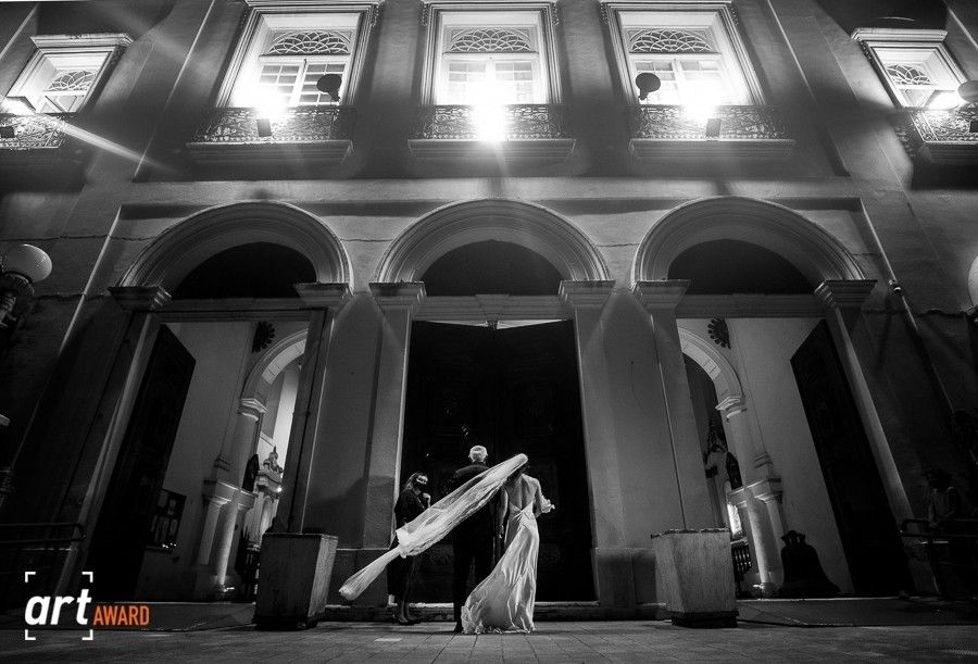 Black and white photo of a bride in a flowing gown entering an elegant arched building at night.