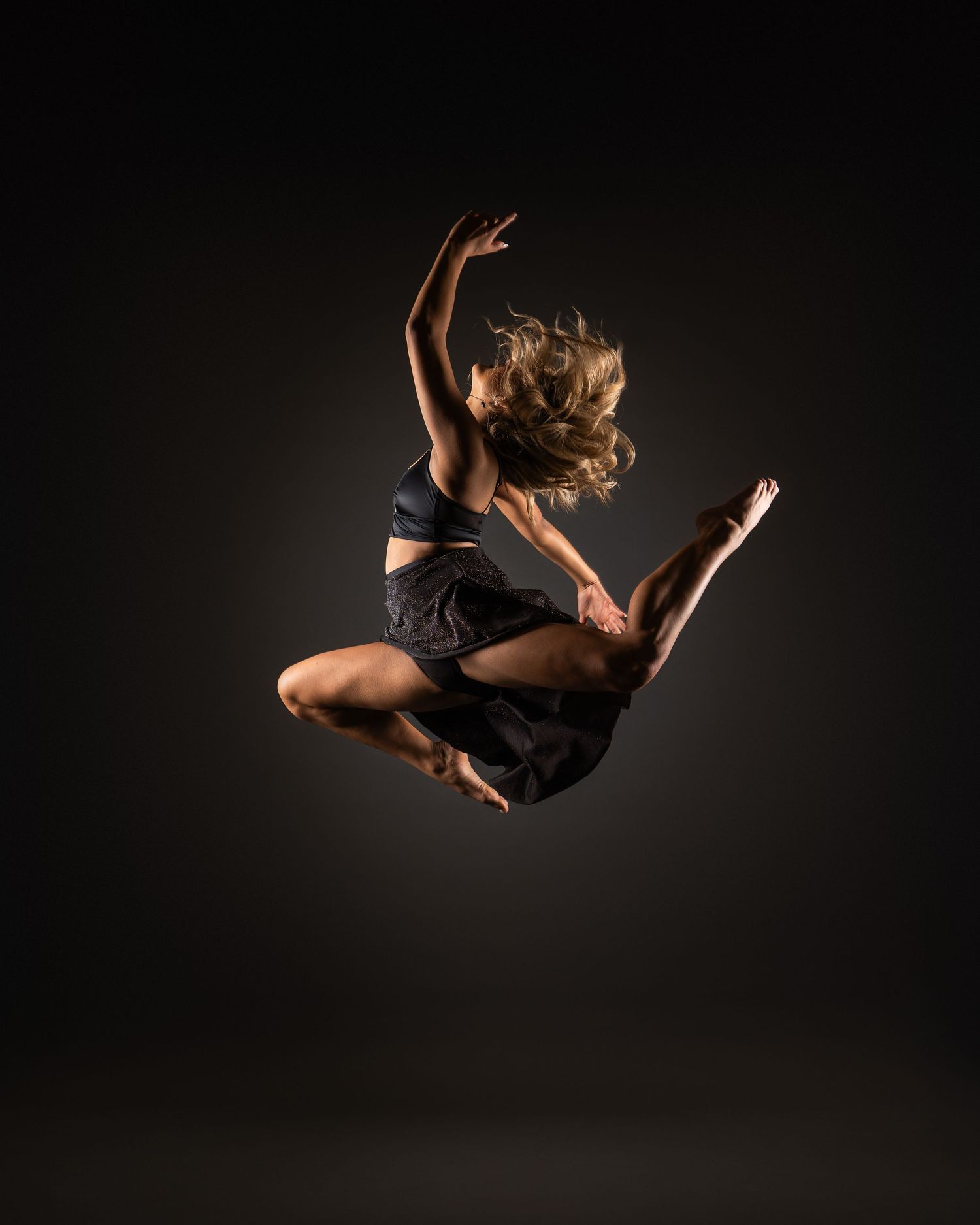 A dancer in black performs a graceful leap against a dark background, creating a dynamic silhouette in motion.
