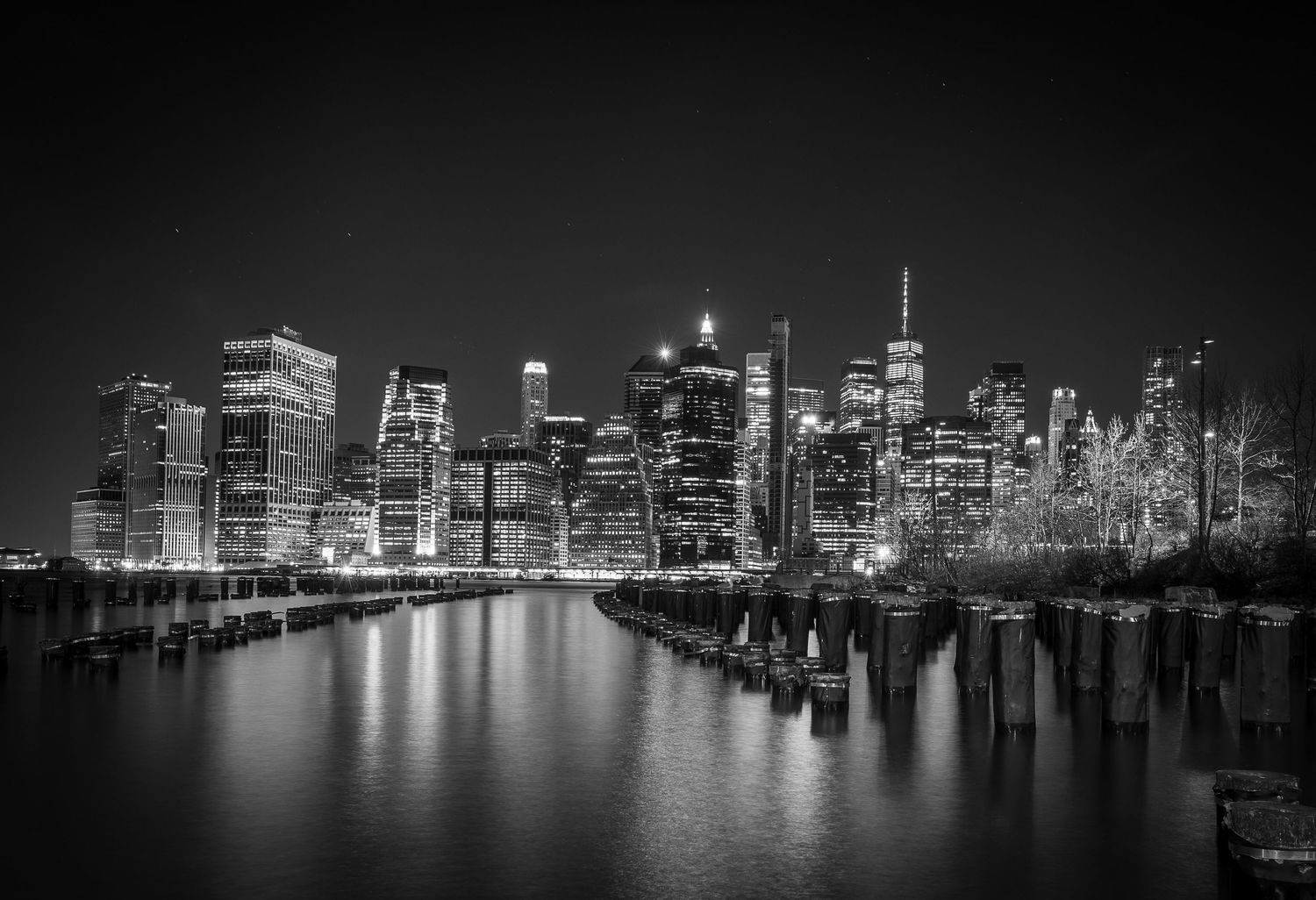 Manhattan skyline reflecting in the East River at night in dramatic black and white.