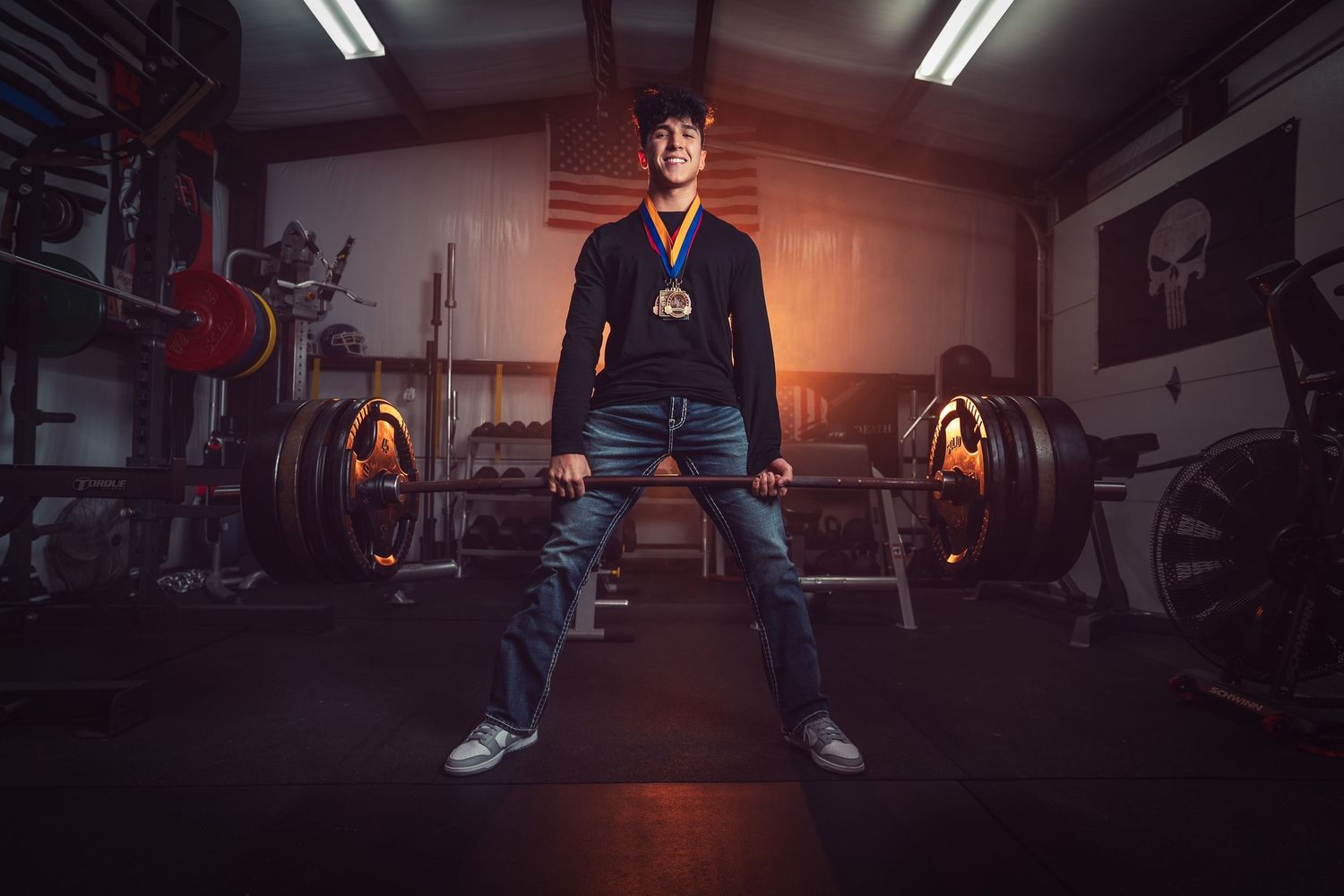 Person stands confidently in a dimly lit gym with dramatic orange lighting and exercise equipment in the background.