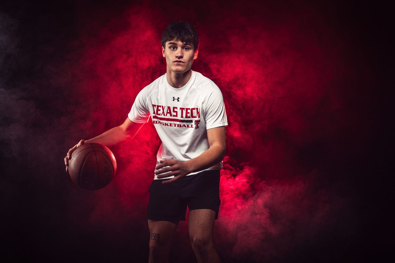 Baseball player in white uniform poses with ball against dramatic red smoke background.