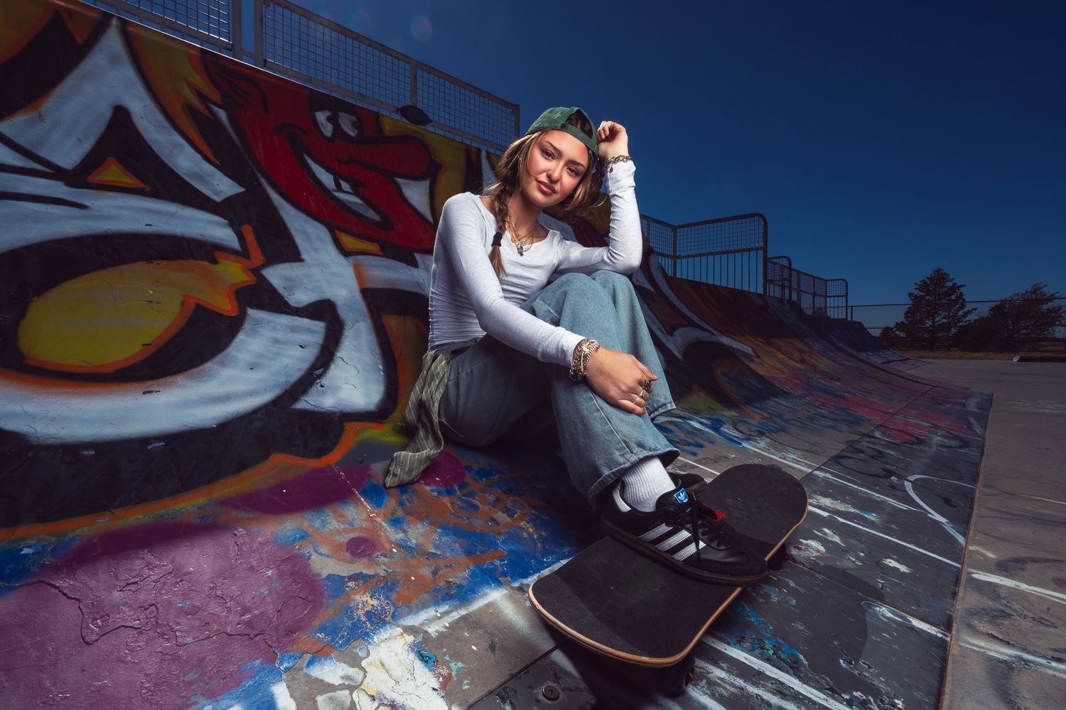 Person in casual wear sitting with a skateboard against colorful graffiti wall on a sunny day.