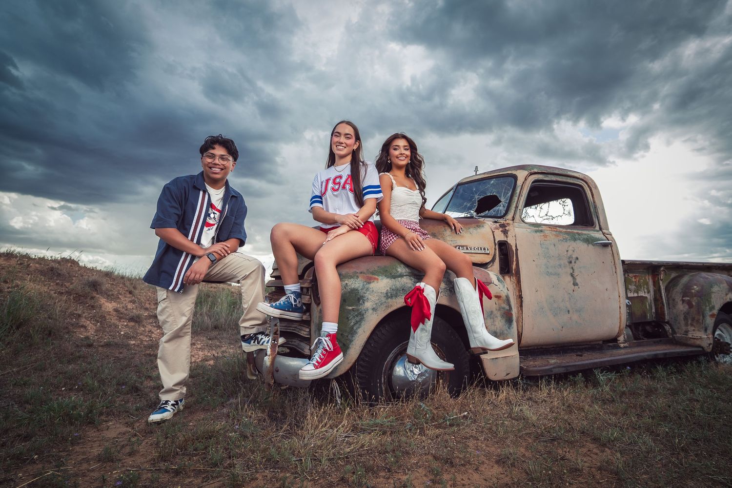 Vintage truck photoshoot with patriotic red white and blue theme against dramatic cloudy sky backdrop.
