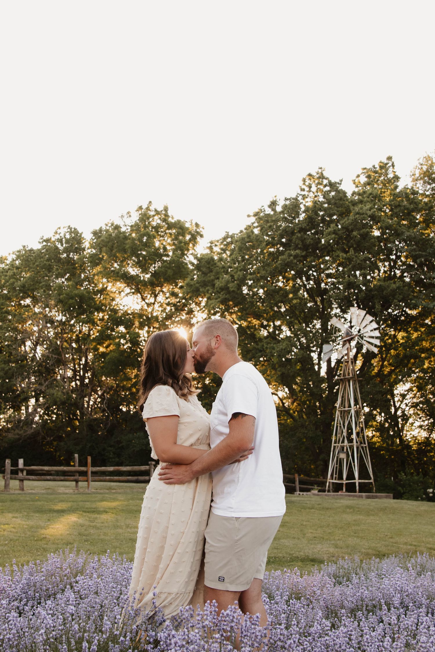 Romantic couple embracing in a lavender field at sunset with a windmill in the background.
