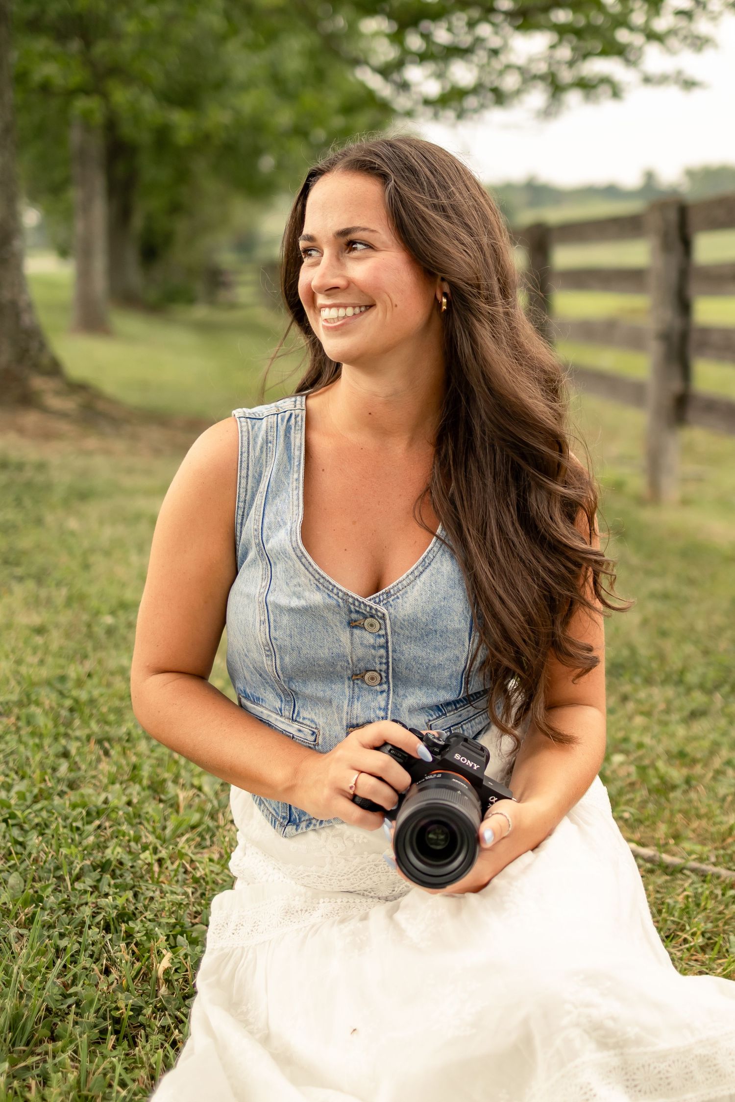 Photographer branding photo by a horse field, sitting in the grass holding a camera